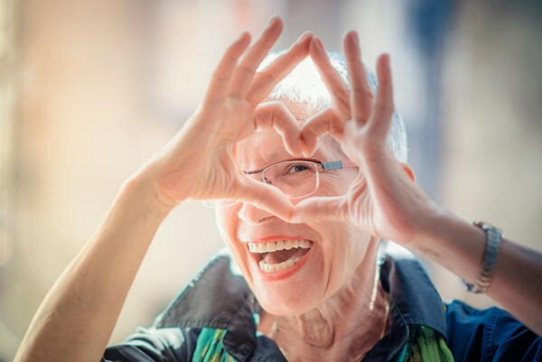 Freundliche ältere Frau, die mit ihren Händen und Fingern eine Herzform macht