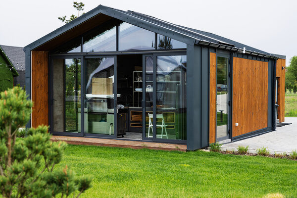 Bild vergr&ouml;&szlig;ern: Modernes Tiny House mit Holzverkleidung, dunklem Stahlrahmen und gro�er Glasfront in einem gr�nen Garten